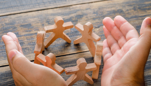 Wooden people figures being protected by human hands