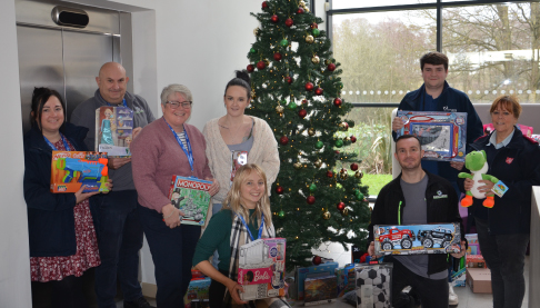 Team members holding gifts and smiling in front of a Christmas tree.